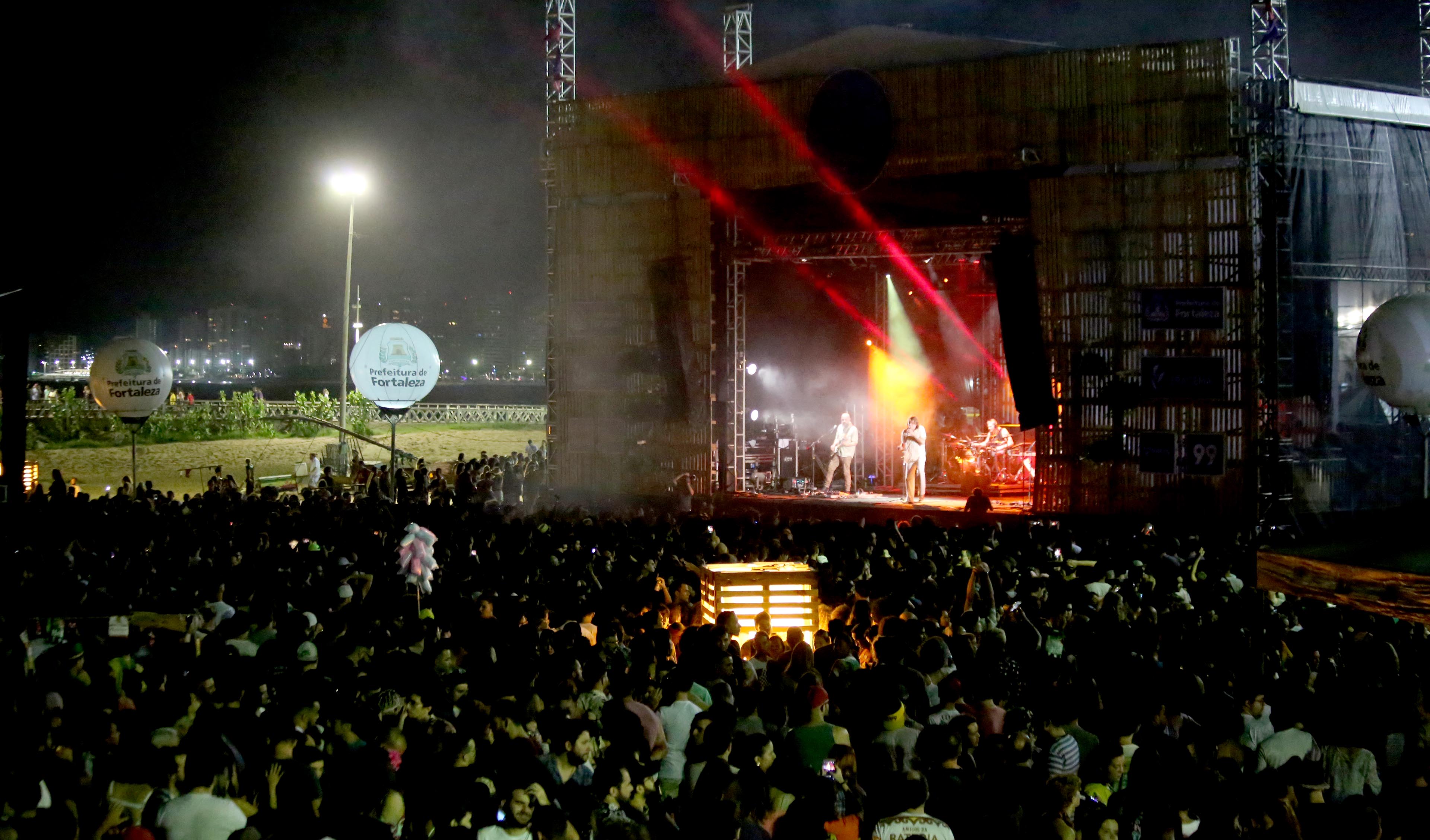 a foto mostra o palco de shows montado na praia de iracema, com público assistindo